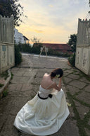 Person in a Vogsion Élodie Lace Corset Bow Satin Maxi Dress sitting on a stone path with a sunset in the background