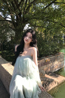 Woman in a light green Vogsion Seraphina Tiered Chantilly Lace Maxi Dress standing by a stone wall with trees in the background