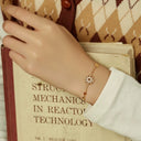 Hand wearing a gold bracelet on an open book with a patterned fabric background