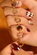 Close-up of a hand holding a gold bracelet with brown beads against a blurred background