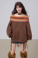 Woman wearing a brown sweater with a patterned neckline and fringed skirt on a plain background