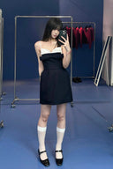 Woman taking a mirror selfie wearing Vogsion Antoinette Structured Bow Tailored Mini Dress and white socks in a room with blue walls and clothing racks.