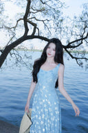 Woman in a Vogsion Light Blue Floral Maxi Dress standing by a body of water with trees in the background