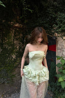 Woman wearing a Vogsion Pistachio Green Strapless Corset Ruffle Peplum Lace Prom Dress 2026 with ruffles in an outdoor setting.