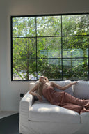 Woman wears  Vogsion Strapless Twist Knot Satin Draped Maxi Dress lying on a white couch in a room with large windows showing greenery outside.