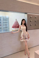Woman in a floral dress standing in front of a display case with a pink cake-like display.