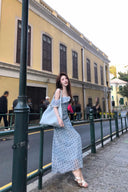 Woman in a Vogsion L’Avenir Polka-Dot Lace Ruffle Maxi Dress in Powder Blue standing on a street with a building in the background