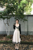 Woman in a Vogsion "Lucienne" Ethereal Tulle & Contrast Lace-Inset Midi Dress with black floral details standing outdoors against a wall with greenery.