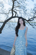 Woman in a Vogsion Light Blue Floral Maxi Dress standing by a body of water with trees in the background