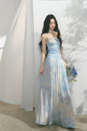 Woman in a light blue strapless dress holding flowers against a white curtain background