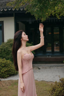 Vogsion blush corset maxi dress side profile reaching toward leaves outdoors