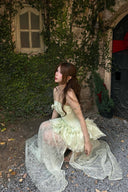 Woman in a Vogsion Pistachio Green Strapless Corset Ruffle Peplum Lace Prom Dress 2026 sitting on a gravel path with ivy-covered walls in the background
