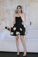 Woman in a Vogsion Midnight Bloom Architectural Mini Dress with white floral details standing against a neutral wall.