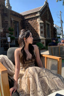Woman wearing the VOGSION Luna Twist Midi Dress in Cream Perla Paisley silk-linen fabric, featuring a voluminous flare skirt and waist cut-out in a lush garden setting