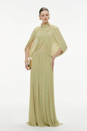 Woman wearing a Vogsion Light Pomelo Olive Mesh Knit Draped Cape Pleated Maxi Dress with a cape on a white background