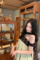 Woman in a Vogsion Velvandis Off Shoulder Dot Mini Dress sage green polka dot with a black polka dot scarf in a room with wooden shelves.