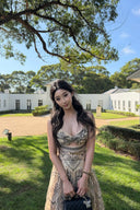 Woman wearing the VOGSION Luna Twist Midi Dress in Cream Perla Paisley silk-linen fabric, featuring a voluminous flare skirt and waist cut-out in a lush garden setting