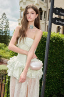 Woman in a Vogsion Pistachio Green Strapless Corset Ruffle Peplum Lace Prom Dress 2026 standing outdoors near a building with directional signs.