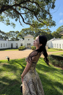 Woman wearing the VOGSION Luna Twist Midi Dress in Cream Perla Paisley silk-linen fabric, featuring a voluminous flare skirt and waist cut-out in a lush garden setting