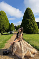 Woman wearing the VOGSION Luna Twist Midi Dress in Cream Perla Paisley silk-linen fabric, featuring a voluminous flare skirt and waist cut-out in a lush garden setting