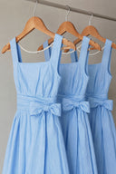 Azure Linen Sky-Blue/Beige A-Line Backless Pearl Wide-Leg Jumpsuit displayed on wooden hangers, showcasing the square neckline, pearl back chain, waist bow and relaxed wide-leg silhouette