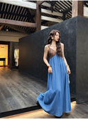Woman in a blue dress standing in a room with wooden floors and dark walls.