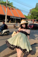 Woman in a Vogsion Velvandis Off Shoulder Dot Mini Dress sage green polka dot and hat standing on a street with 'Blue Coffee' in the background
