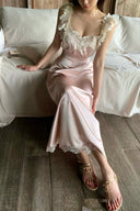 Woman in Vogsion Sunset Aurelia Lace-Trimmed Liquid Satin Gown – Champagne Pink Resort Maxi Slip Dress sitting on a bed in a bedroom setting