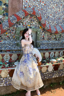 Vogsion Dawning Floral Corset Midi Dress featuring a blue and white boho floral pattern and tie straps, shown on a customer in a scenic vacation setting