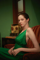 Woman in a green dress sitting on a red couch in a room with green walls.