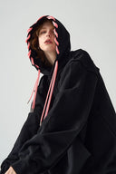 Person wearing a black hoodie with pink drawstrings on a light gray background
