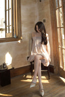 Vogsion Neutral Draped Glossy Mini Dress - A high-shine champagne off-the-shoulder dress with sculptural draping and cape sleeves worn by a Vogsion customer