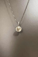 Necklace with a shell pendant featuring a pearl on a gray background