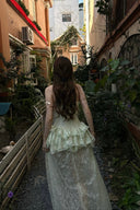 Woman in Vogsion Pistachio Green Strapless Corset Ruffle Peplum Lace Prom Dress 2026 walking through a narrow alleyway with plants and buildings.