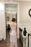 Woman in Vogsion Élodie Bow-Tiered Ivory Lace Maxi Dress standing in a home interior with wooden floors and a staircase.