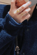 Hand wearing Vogsion Le Brunch Croissant Shell Adjustable Ring with a blue coat and black handbag in the background