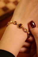 Gold bracelet with a tiger's eye stone on a wrist against a blurred background
