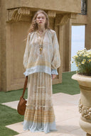 Woman in Vogsion Tiered Pleated Lace-Trimmed Printed Silk Maxi Skirt standing in an outdoor setting with classical architecture.