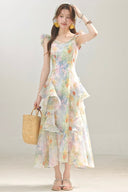 Woman wearing a Vogsion Watercolor Cascade tiered ruffle dress holding a straw bag against a plain background