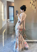 A woman wearing the Vogsion Bias Maxi Dress in Rose Garden Revolution, a pink and beige floral print dress with a ruffled mermaid hem and V-neckline, showcased by a real Vogsion customer
