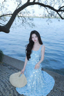 Woman in a Vogsion Light Blue Floral Maxi Dress s standing by a body of water with trees in the background