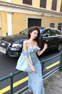 Woman in a light blue dress standing on a street with a black Audi car in the background.