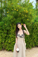 Woman in Vogsion "Lucienne" Ethereal Tulle & Contrast Lace-Inset Midi Dress standing in front of green foliage with yellow flowers.