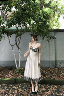 Woman in Vogsion "Lucienne" Ethereal Tulle & Contrast Lace-Inset Midi Dress with black lace details standing outdoors near a tree and wall.