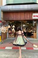 Woman wear Vogsion Velvandis Off Shoulder Dot Mini Dress sage green polka dot walking past a hat shop with various hats displayed outside.