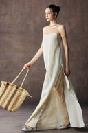 Woman in a Vogsion Architectural Column Gown in sand holding a woven basket against a brown background