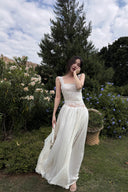 Woman in a Vogsion Amber Light Lace Spliced Open Back Tie Strap Maxi Dress standing in a garden with trees and flowers in the background