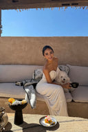 Woman in a Vogsion ivory strapless cut out ruched maxi dress sitting on a couch with a dog, holding a cup, on a sunny day.