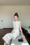 Woman in a Vogsion Shush TrongWhite Linen Statement Bow Petite Midi Dress sitting on a checkered floor in a minimalistic room.