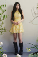 Vogsion Aurelia Soleil Floral Mini Dress worn by a normal customer in a botanical studio, high-end A-line silhouette, luxury yellow floral fashion, authentic customer photo.